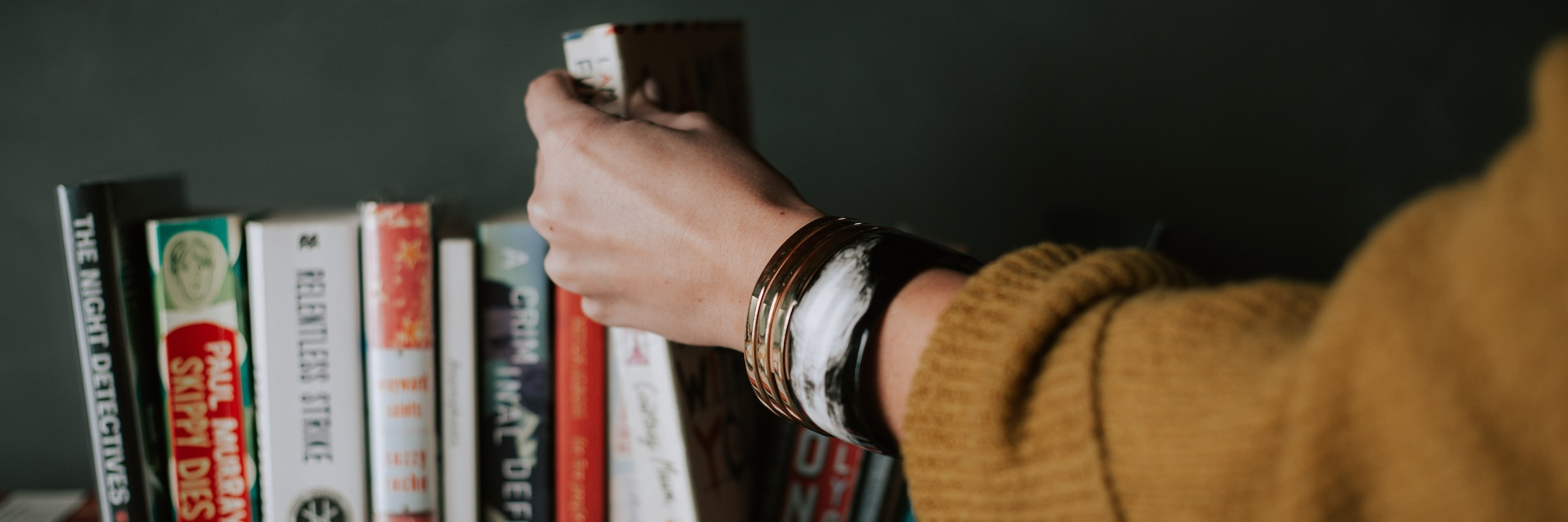 Closeup of bookshelf and arm of person browsing